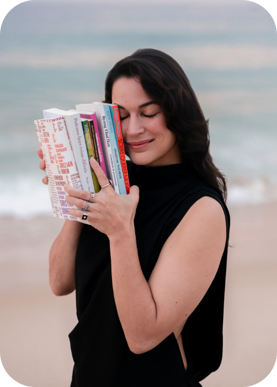 Karina Francis abraçada a uma pilha de livros na praia