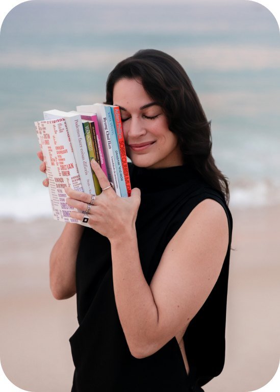 Karina Francis abraçada a uma pilha de livros na praia